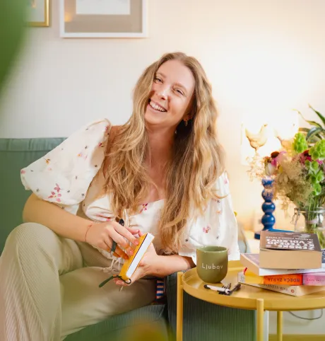 Mateja on her couch, laughing, with books and a mug on the side table